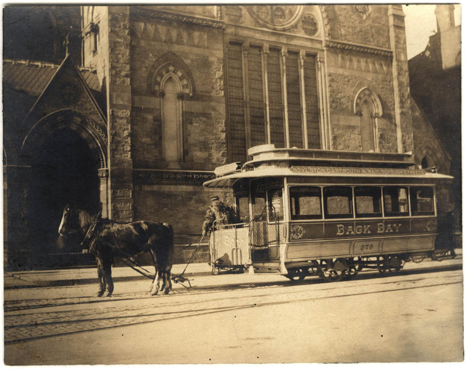 Reddish-brown photograph of a horse-drawn streetcar in front of a church
