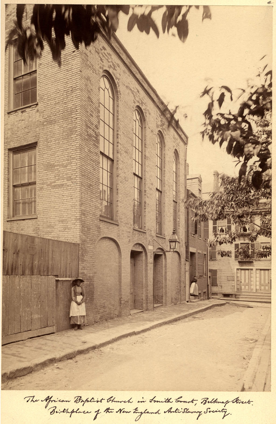 a sepia-toned photograph of a tall building and two women standing on the sidewalk outside of it