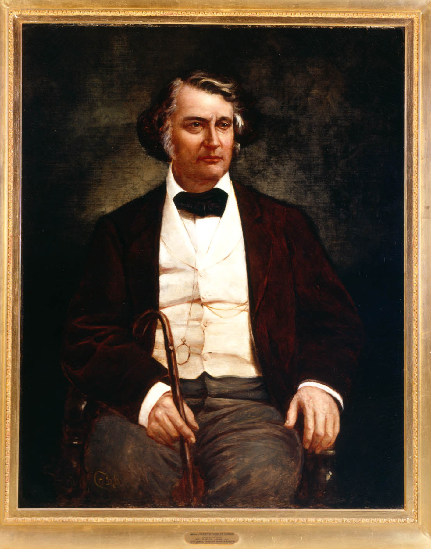 a painted portrait of a seated white man with gray hair wearing a black jacket and bow tie, white collared shirt and tweed pants, in a gold frame