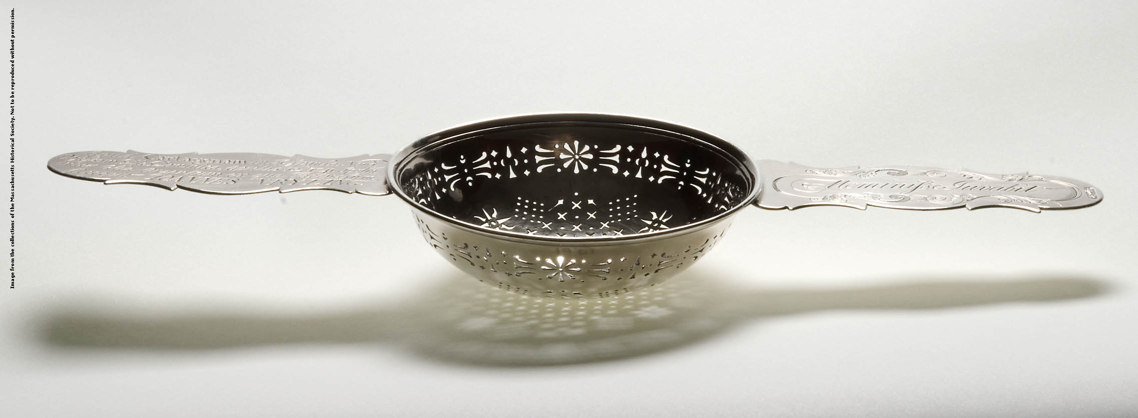 a silver punch strainer with long handles casts a shadow over a white surface