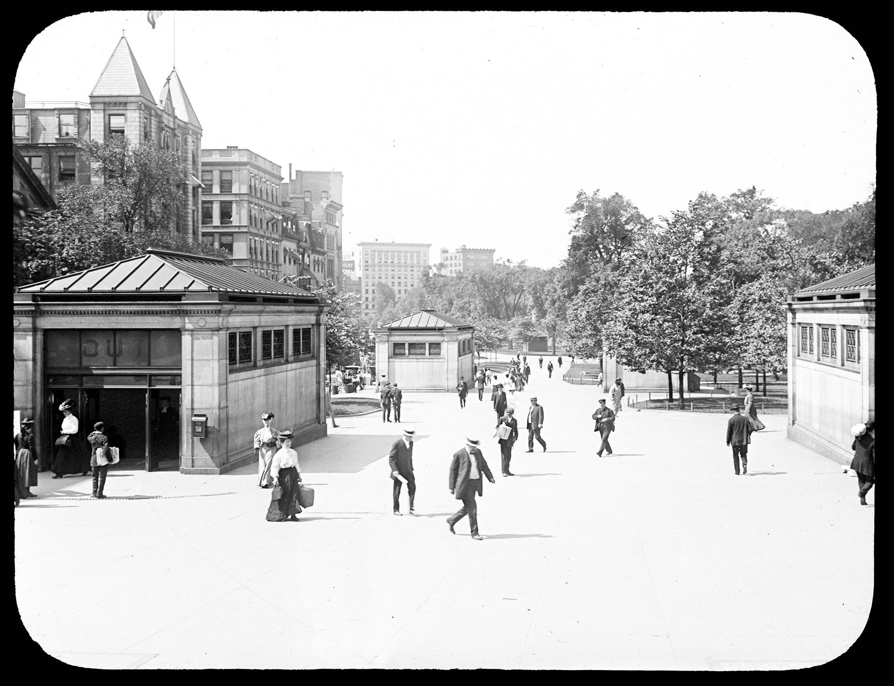 Black and white photograph depicting a subway entrance with many well-dressed men and women walking past. The photo also shows two young boys selling newspapers to the passing crowd